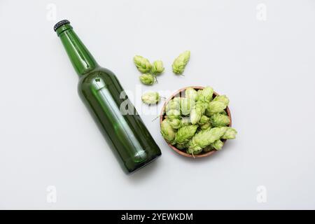 Schüssel mit grünen Hopfenkegeln und Flasche Bier auf weißem Hintergrund Stockfoto