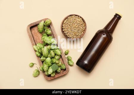 Brett mit grünen Hopfenkegeln, Samen und Flasche Bier auf beigefarbenem Hintergrund Stockfoto