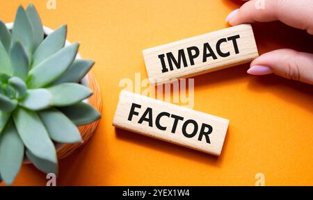 Symbol für Aufprallfaktor. Holzblöcke mit den Worten Impact Factor. Schöner oranger Hintergrund mit saftiger Pflanze. Geschäftsmann Hand. Business und Impact Stockfoto