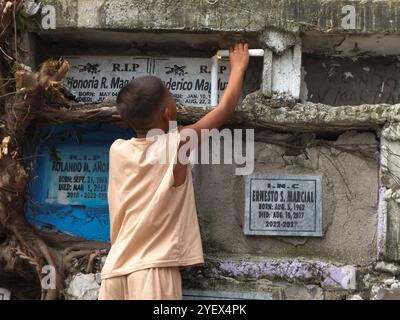 Navotas, Philippinen. November 2024. Ein kleiner Junge zündet eine Kerze am Grab seines verstorbenen Verwandten an. Filipinos strömen zu verschiedenen Friedhöfen, um UNDAS oder Allerheiligen in verschiedenen Teilen der Philippinen zu begehen. Sie bieten Blumen und Kerzen an, die an die Gräber ihrer verstorbenen Verwandten gelegt werden. Quelle: SOPA Images Limited/Alamy Live News Stockfoto