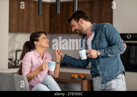 Ein fröhliches Paar teilt sich einen Moment des Lachens bei einem Morgenkaffee in einer modernen Küche mit Wärme und Verbundenheit. Entspannung und Glück sind das Stockfoto