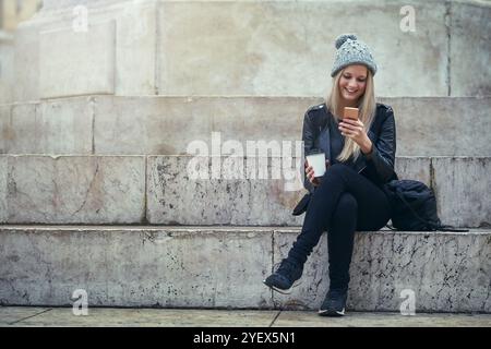 Lachen, Kaffee oder glückliche Frau in der Stadt mit Telefon in sozialen Medien, im Internet oder Blog für Modetipps. Stadt, Drink oder trendiges Mädchen Stockfoto