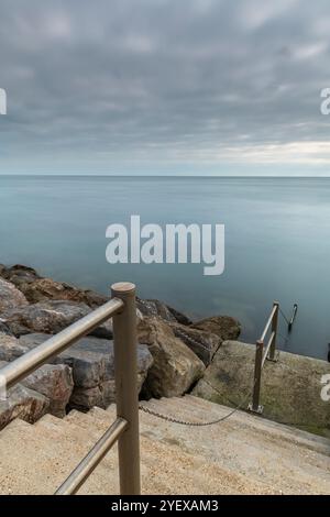 Steintreppen führen hinunter zum Meer in einer stimmungsvollen und stimmungsvollen Meereslandschaft, die den Eindruck von Abgeschiedenheit oder Stille und Verödung vermittelt. Stockfoto