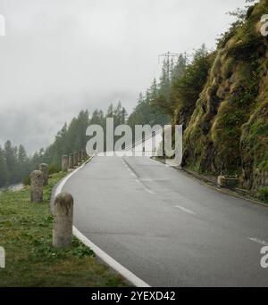 Leere Tremola Bergstraße an einem nebeligen Tag. Kurviger Alpenpass der Lepontinischen Alpen im Kanton Tessin, Kiefernwald am Berghang. Stockfoto