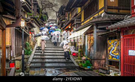 Düsterer, regnerischer Tag in Japan. Treppen mit Menschen und Sonnenschirmen führen durch ein Einkaufsviertel zu einem Tempel. Stockfoto