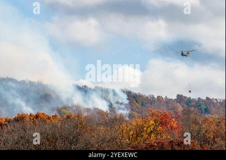 Ein CH-47 Chinook Hubschrauber, der zum 169. Aviation Regiment der Connecticut National Guard gehört, bereitet sich darauf vor, einen Bambi-Eimer mit Wasser auf ein Brushfire zu werfen, das am Lamentation Mountain in Berlin, Connecticut, 23. Oktober 2024, brennt. Dies war das erste Mal seit 1995, dass Flugzeuge der Connecticut National Guard eine Luftfeuerwehrmission im Bundesstaat durchführten. Stockfoto