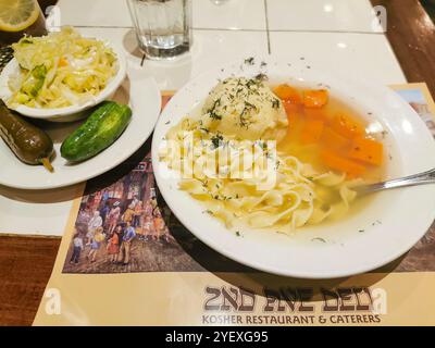 Ein Teller Matzah-Ball-Suppe mit Nudeln, Karotten und einer Seite Krautsalat und Gurken im berühmten 2nd Avenue Deli in NYC. Stockfoto