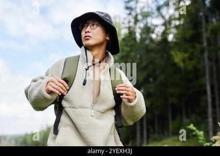 Flaches Porträt eines asiatischen Mannes mit Rucksack, der das Wandern in der Natur genießt, selbstbewusst vor blauem Himmel steht und wegblickt Stockfoto