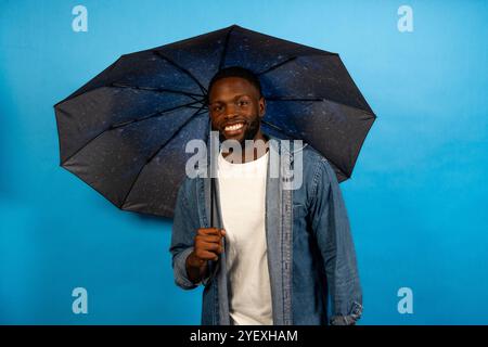 Lächelnder schwarzer Mann mit Schirm isoliert auf blauem Hintergrund Stockfoto Lächelnder schwarzer Mann mit Schirm isoliert auf blauem Hintergrund Stockfoto