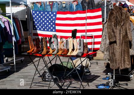 Sammlung von Cowboystiefeln auf einem Tisch mit einer großen amerikanischen Stern- und Streifenfahne im Hintergrund DUMBO Outdoor Flohmarkt New york usa Stockfoto