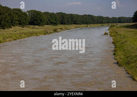 Nach starken Regenfällen überströmt der Fluss in der Stadtlandschaft mit starken Strömungen und schlammigen Gewässern entlang grasbewachsener Ufer Stockfoto