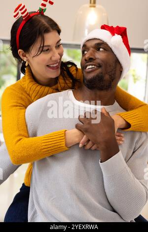 Lächelndes multirassisches Paar, das zu Hause Weihnachten feiert und festliche Hüte und Pullover trägt Stockfoto