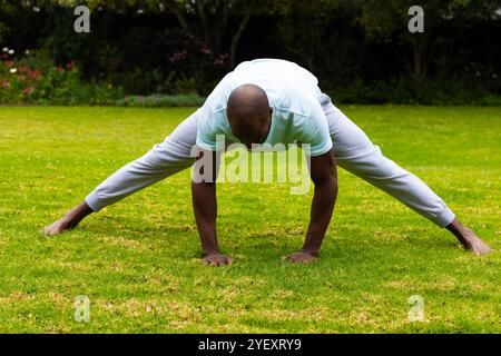 afroamerikanischer Mann, der sich im Park auf Gras ausdehnt und sich auf Fitness und Flexibilität konzentriert Stockfoto