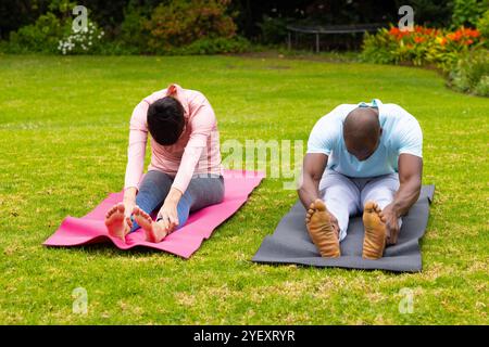 Multiethnische Paare üben Yoga auf Matten im Garten, dehnen und entspannen im Freien Stockfoto