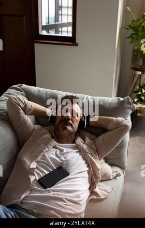Entspannen Sie sich zu Hause, ein älterer Mann genießt Musik mit Kopfhörern auf dem Sofa Stockfoto