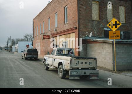 Ein alter Jeep-Truck steht in einer ruhigen Straße neben einem Gebäude mit einem Coors-Schild unter dem No Train Horn-Schild in Brush, Colorado. Stockfoto
