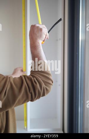 Mann, der die Wand mit einem Maßband misst Stockfoto