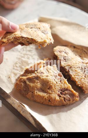 Köstlich frisch gebackene Plätzchen auf Pergamentpapier mit einer Hand, die ein Stück hält Stockfoto