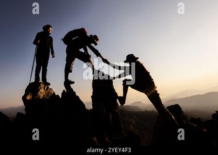 Silhouette von Wanderer, die Bergklippen hochklettern. Die Klettergruppe hilft sich gegenseitig, während sie bei Sonnenuntergang aufsteigt. Konzept von Hilfe und Teamarbeit. Stockfoto