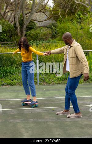 Skateboarden draußen, multirassisches Paar hält Hände und balanciert zusammen im Park Stockfoto