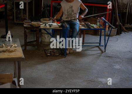 Murano Glasbläserei. Gebläse bildet ein wunderschönes Stück Glas: Legen Sie einen Eisenstab mit befestigtem Glasgegenstand in den Ofen, um das Glas verformbar zu machen. Stockfoto