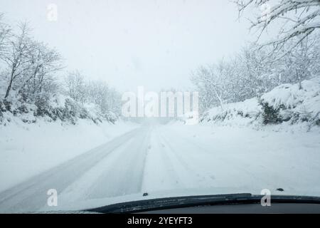 Bild einer Landstraße während eines Schneefalls aus dem Inneren eines Autos. Fahrzeug auf der Straße bei starkem Schneefall, aus Sicht des Fahrersitzes Stockfoto