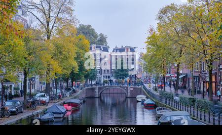 Amsterdam 23. Oktober 2024, goldene Herbstblätter umrahmen die ruhigen Kanäle Amsterdams, während Boote sanft auf dem Wasser schweben und Fußgänger durch die bezaubernden Straßen schlendern Stockfoto