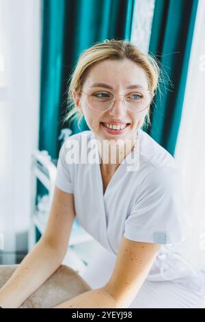 Eine junge Ärztin in einem weißen medizinischen Anzug sitzt im Büro und wartet auf einen Patienten. Dermatarztpraxis Stockfoto