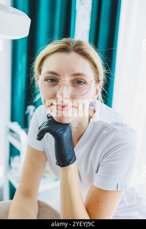 Eine junge Ärztin in einem weißen medizinischen Anzug sitzt im Büro und wartet auf einen Patienten. Dermatarztpraxis Stockfoto