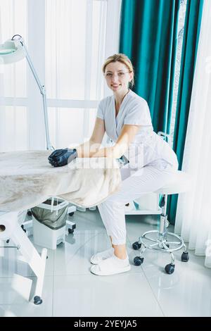 Eine junge Ärztin in einem weißen medizinischen Anzug sitzt im Büro und wartet auf einen Patienten. Dermatarztpraxis Stockfoto