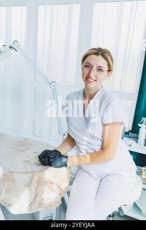 Eine junge Ärztin in einem weißen medizinischen Anzug sitzt im Büro und wartet auf einen Patienten. Dermatarztpraxis Stockfoto