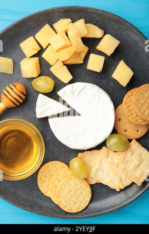 Käseplatte mit verschiedenen Käse, Cracker, Trauben und Honig auf dunklem Teller. Vertikales Foto Stockfoto