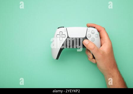 Mykolaiv, UKRAINE - Juli 2024: Weibliche Hand mit einer neuen Sony PlayStation auf MINT-Hintergrund. Stockfoto