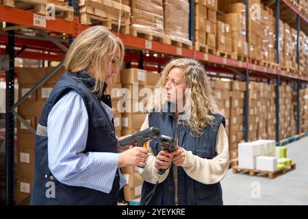 Lagerarbeiterinnen diskutieren über den Einsatz von Barcode-Scannern in Logistikzentren Stockfoto