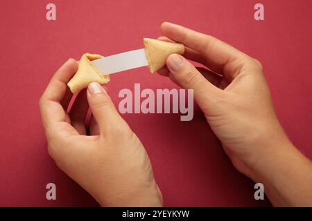 Frau mit leckerem Glückskeks und Papier mit Vorhersage auf rotem Hintergrund. Stockfoto