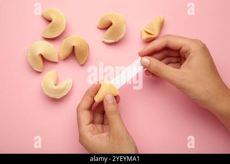 Frau mit leckerem Glückskeks und Papier mit Vorhersage auf rosa Hintergrund. Stockfoto