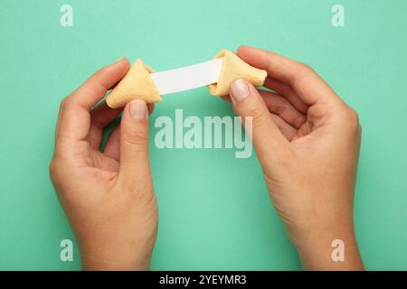 Frau mit leckerem Glückskeks und Papier mit Vorhersage auf MINT-Hintergrund. Stockfoto