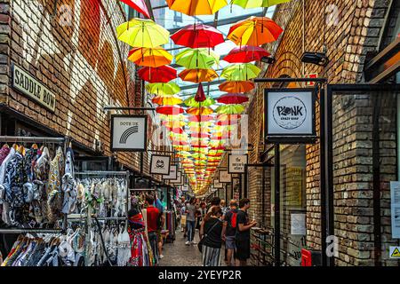 Leute, typische Geschäfte und bunte Regenschirme hängen auf dem Dach des Camden Town Market. London, England, Europa Stockfoto