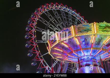 Ein Jahrmarkt bei Nacht mit beleuchtetem Kettenkarussell und Riesenrad, Europa Rad, Fahrten, Wellenflug, Cannstatter Wasen, Volksfest Bad Cannstatt, Stockfoto