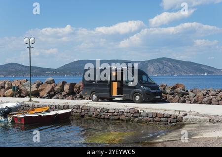 Schwarzer Wohnmobil auf einer Straße mit Blick auf das Meer und die Berge unter blauem Himmel, Wohnmobil, Agios Nikolaos, Agios Nikolaos, Halbinsel Methana Stockfoto