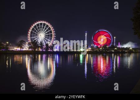 Stimmungsvolle Messe bei Nacht mit hell beleuchtetem Riesenrad und bunten Lichtern im Wasser, Cannstadter Volksfest, Stuttgart, Baden-Wuert Stockfoto