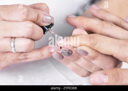 Nahaufnahme eines nagellackers, der nagellack auf den weiblichen Nagel im Nagelsalon aufträgt Stockfoto