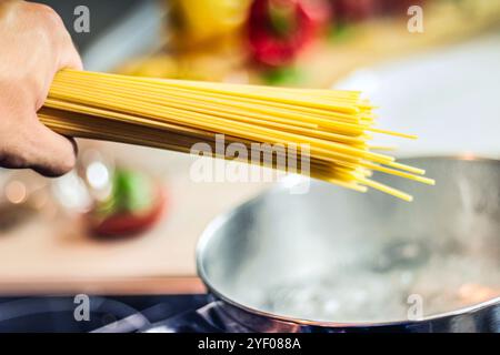 Nahaufnahme der Hand eines weißen Kaukasiers, der trockene Spaghettistangen in einen Topf voller kochendem Wasser steckt Stockfoto