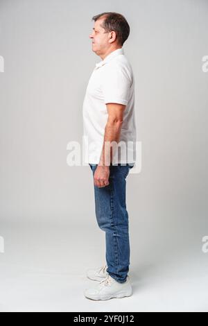 Mann, der seitlich in lässiger Kleidung vor einem schlichten Hintergrund steht Stockfoto
