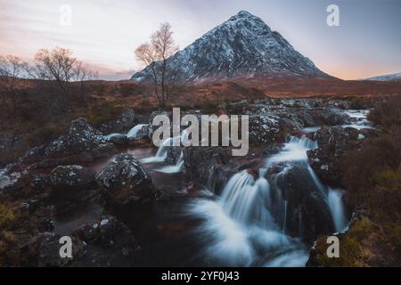 Ein Wasserfall fließt unter dem schneebedeckten Berg Buachaille Etive Mòr in Glencoe, Schottland, und unterstreicht die dramatische Schönheit der Scottis Stockfoto