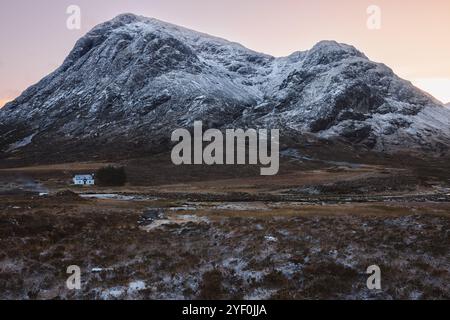 Ein abgelegenes Cottage liegt am Fuße der schneebedeckten Berge in Glencoe, Schottland, und fängt die ruhige Schönheit der schottischen Highlands bei Sonnenuntergang oder Sonne ein Stockfoto
