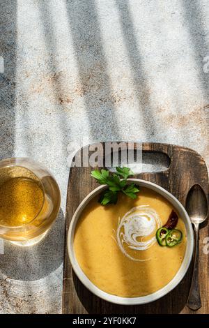 Blick von oben auf eine Schüssel Kürbissuppe auf einem hölzernen Schneidebrett mit einem Glas Weißwein Stockfoto