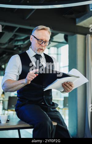 Ein grauer Geschäftsmann, der wichtige Papiere in der Hand hält, ein Mann, der den Vertrag auf Unterschrift überprüft. Arbeiten Sie im Büro Stockfoto