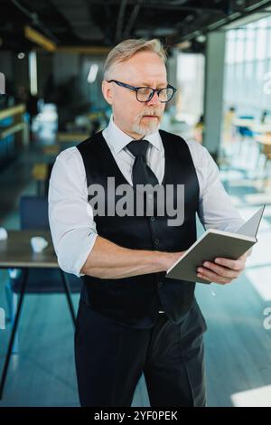 Männlicher Finanzier mit grauem Haar, der Finanzberichte und Verträge überprüft, Erwachsener Chef, der am Arbeitsplatz mit Papieren arbeitet. Stockfoto