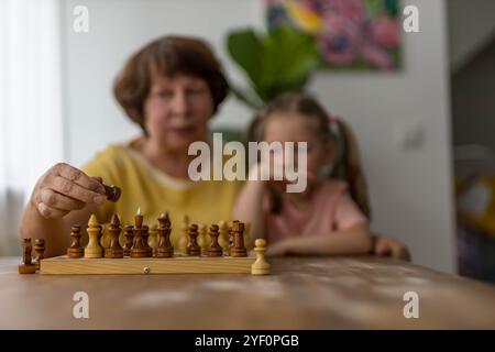 Ein fröhliches Mädchen spielt Schach mit ihrer Großmutter am Tisch und schafft wertvolle Familienerinnerungen. Hochwertige Fotos Stockfoto